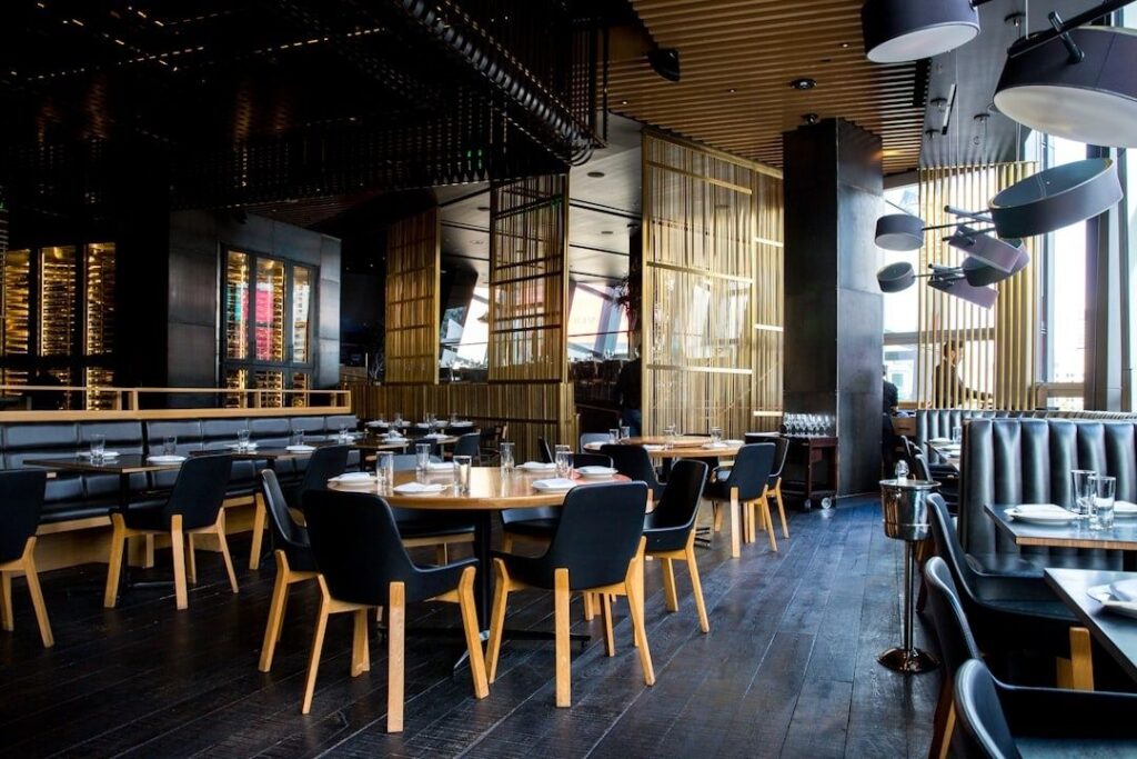 Modern restaurant dining room with tables, booths, and layered ceiling fixtures