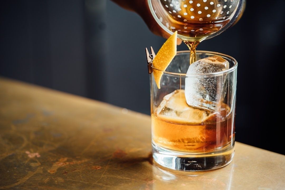 Bartender pours an amber cocktail over ice with an orange garnish