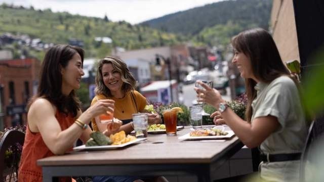 Three women dining outdoors on a terrace overlooking a hillside town