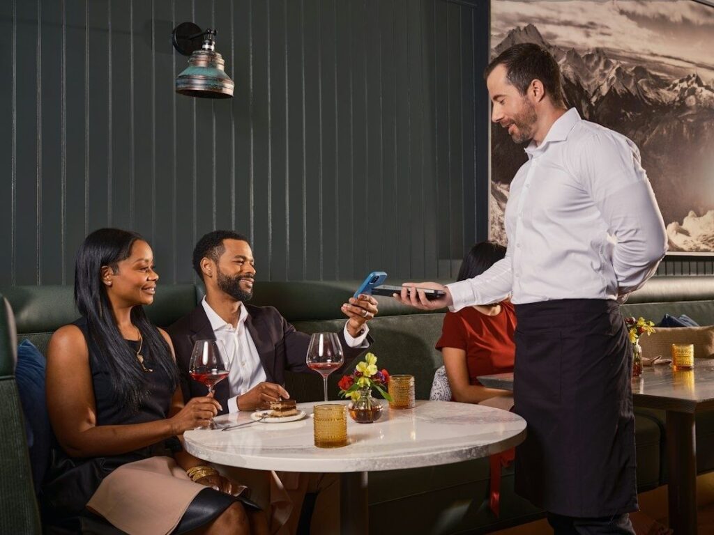 Waiter presents a handheld payment terminal to diners at a restaurant table